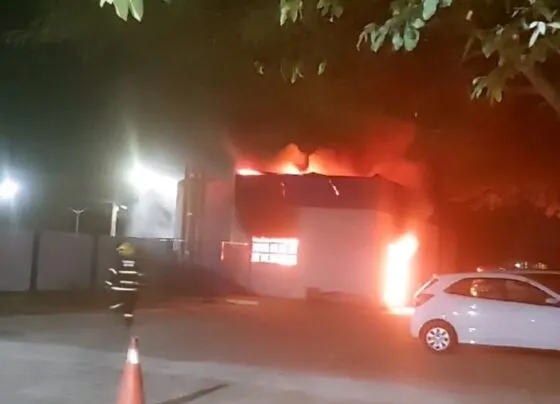 Armazém pegando fogo, carros perto e um bombeiros indo combater o incêndio.