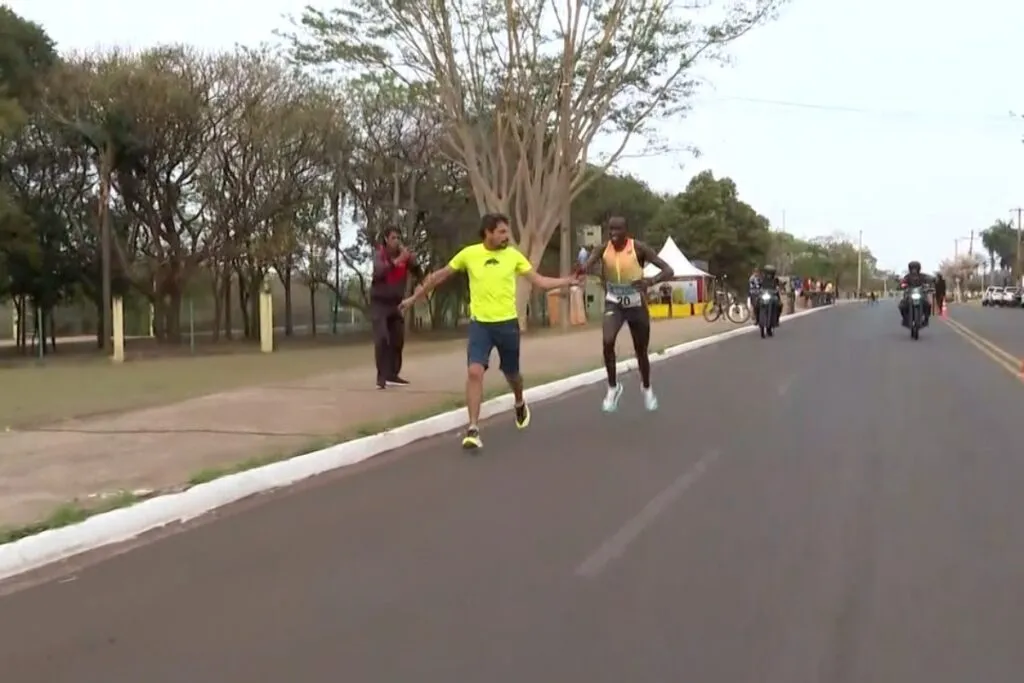 Preparador entregando garrafa com líquido vermelho ao atleta queniano na Corrida do Pantanal (Foto: Magno Lemos/Reprodução)