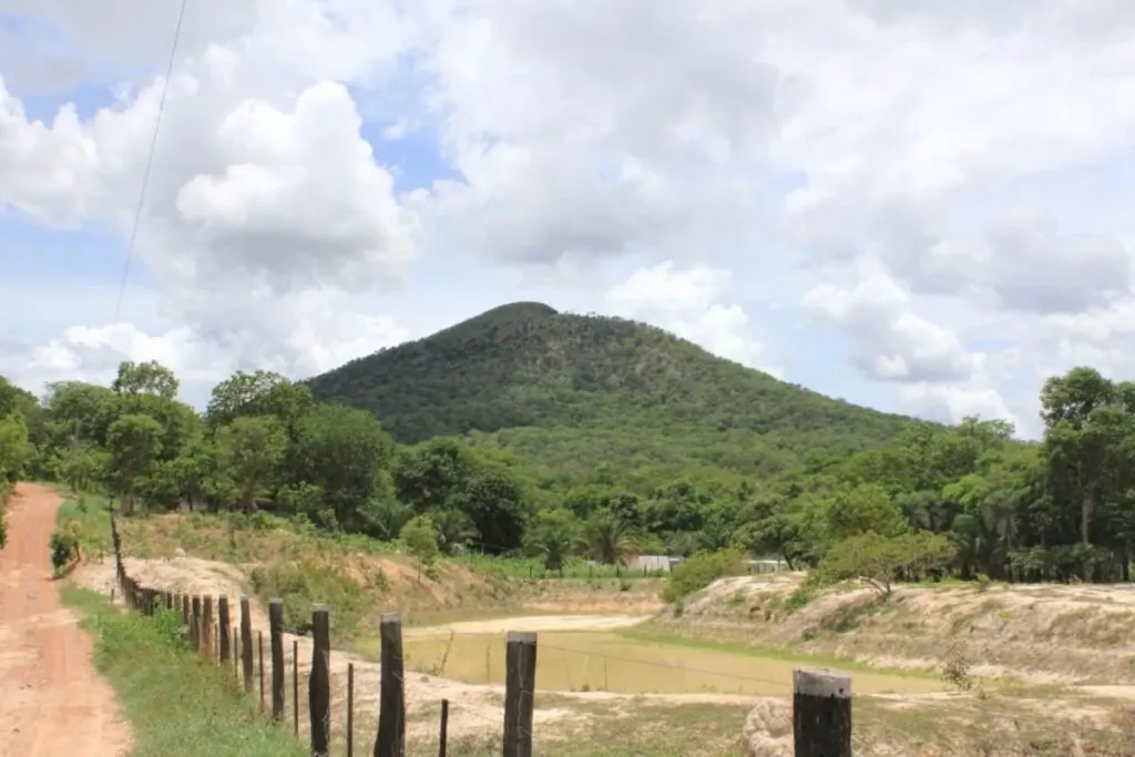 Imagem mostra estrada de terra para Morro de Santo Antônio e morro ao fundo.